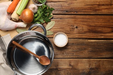 Photo of Pot with ladle and different ingredients for cooking tasty bouillon on wooden table, flat lay. Space for text