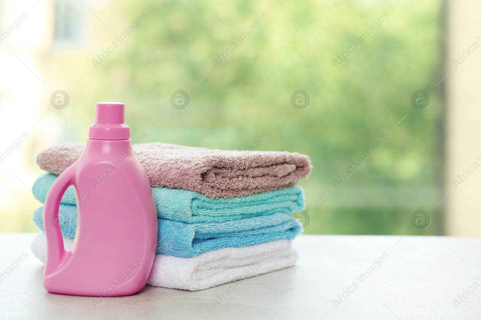 Photo of Stack of clean towels with detergent on table against blurred background. Space for text