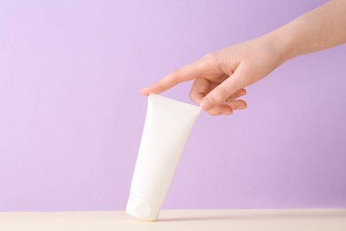 Photo of Woman with tube of cream on lilac background, closeup