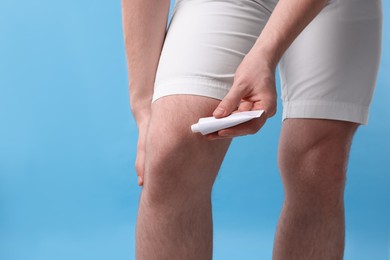 Photo of Man applying ointment from tube onto his knee on light blue background, closeup