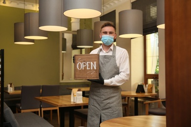 Photo of Waiter with OPEN sign in restaurant. Catering service during coronavirus quarantine