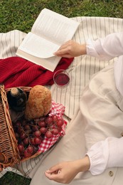 Woman with glass of wine, book and picnic basket on green grass, above view