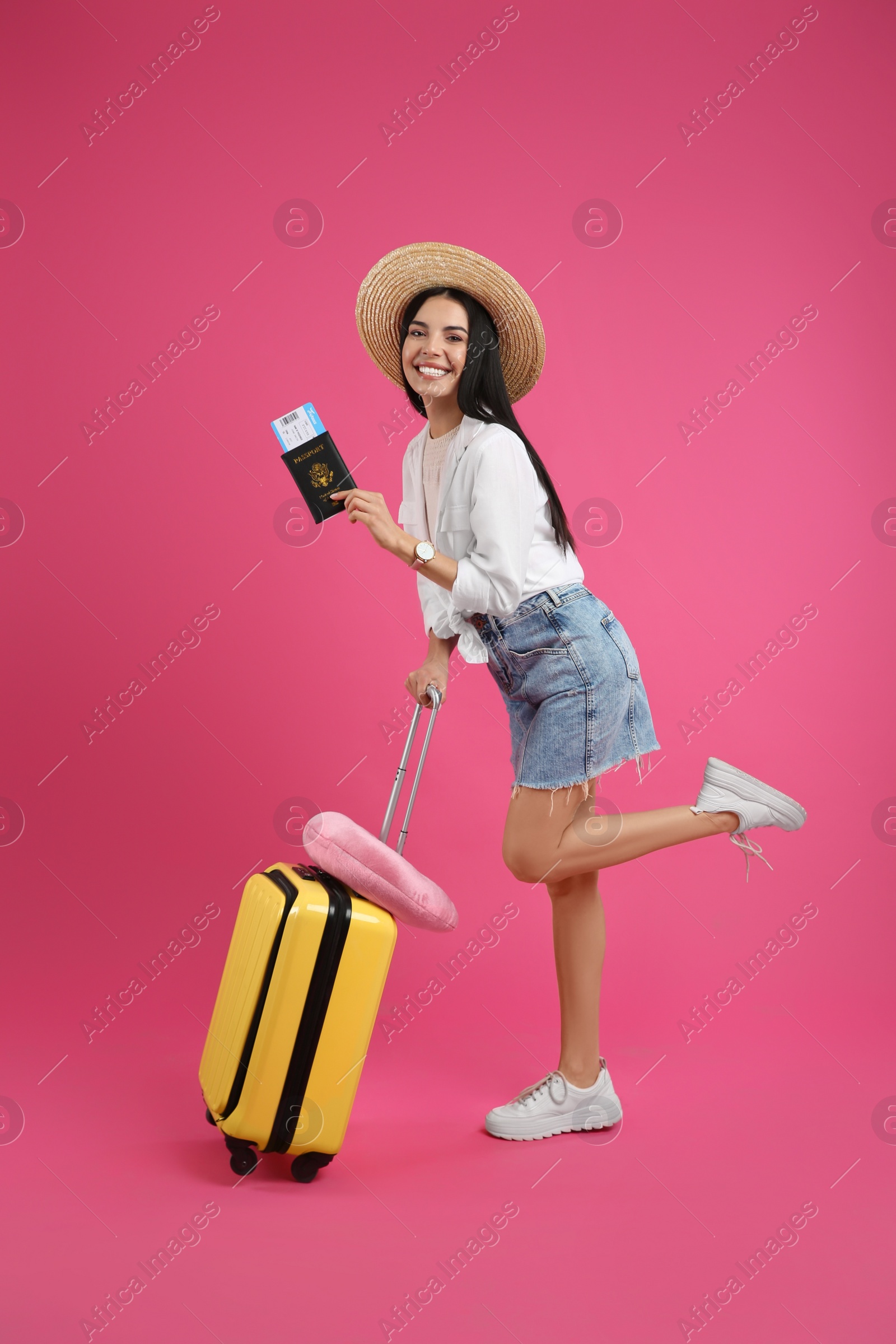 Photo of Happy female tourist with suitcase, ticket and passport on pink background