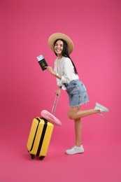 Happy female tourist with suitcase, ticket and passport on pink background