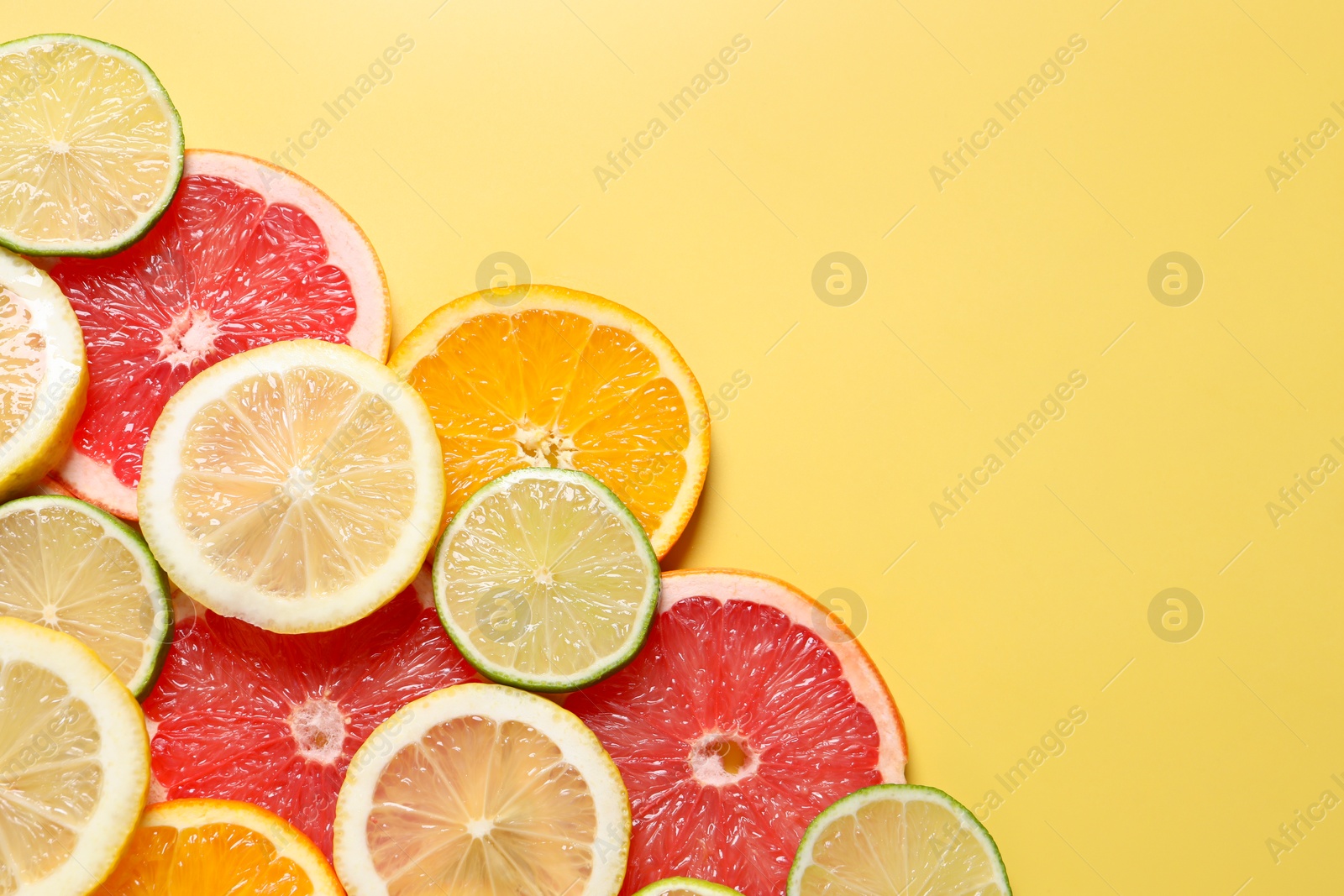 Photo of Different sliced citrus fruits on yellow table, top view. Space for text