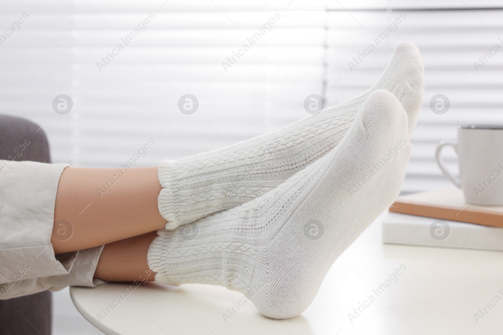 Photo of Woman in warm socks relaxing near table at home, closeup