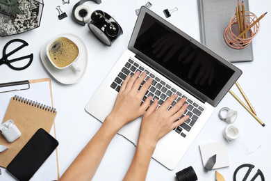 Female designer working with laptop at white table, top view