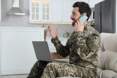 Photo of Happy soldier with laptop talking on phone at home. Military service