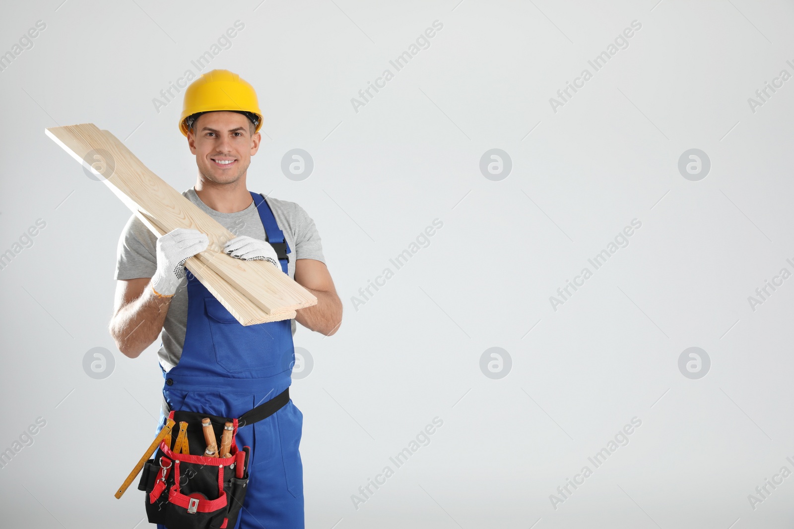 Photo of Handsome carpenter with wooden planks on light background. Space for text