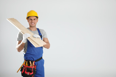 Photo of Handsome carpenter with wooden planks on light background. Space for text