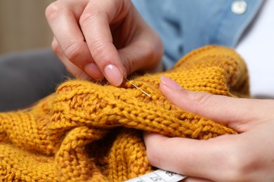 Woman sewing sweater with needle, closeup view