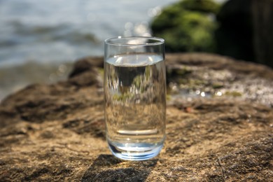Photo of Glass of fresh water on stone near sea