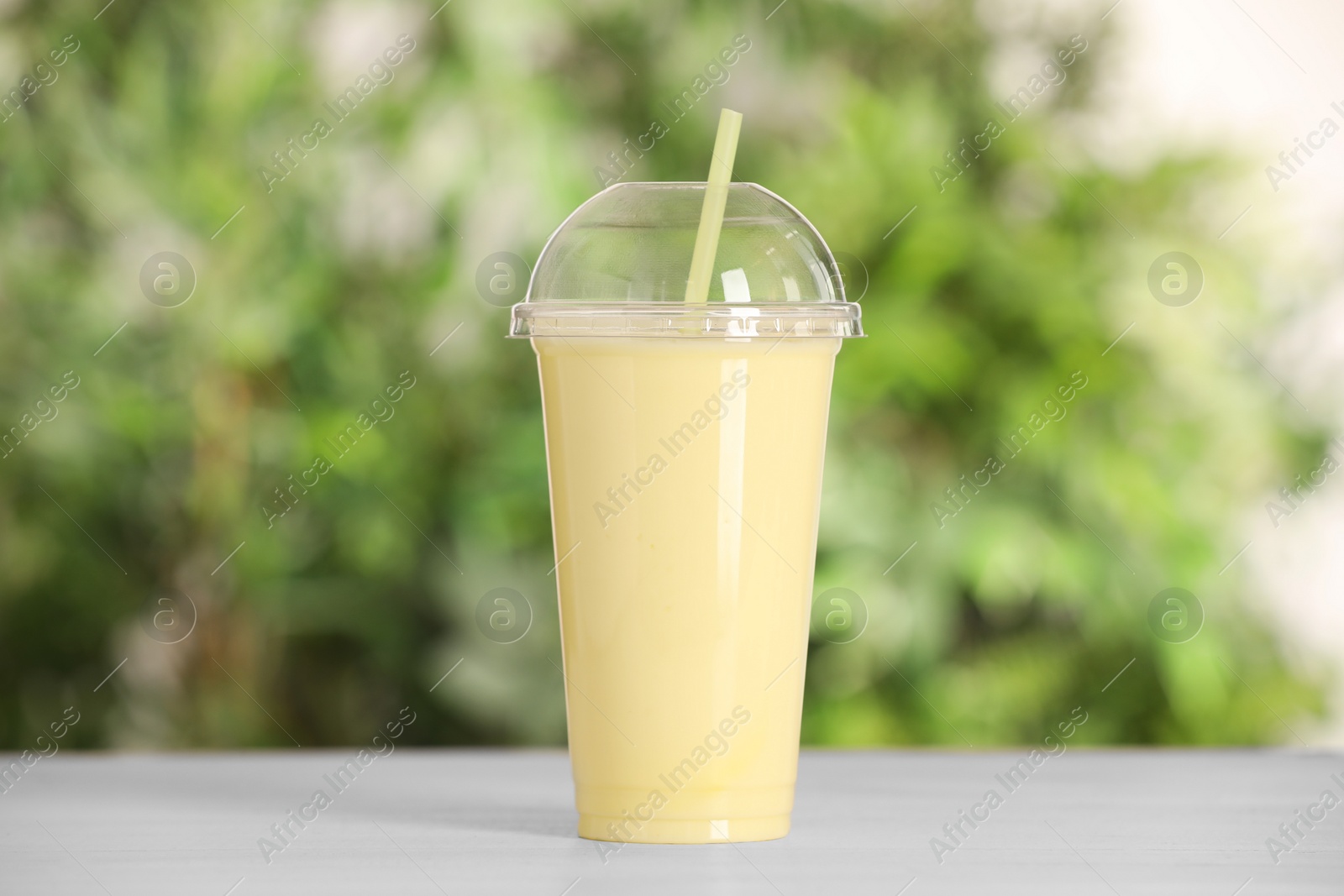 Photo of Plastic cup of tasty smoothie on wooden table outdoors