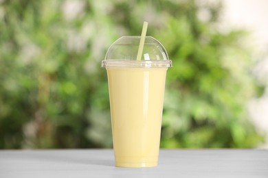 Photo of Plastic cup of tasty smoothie on wooden table outdoors