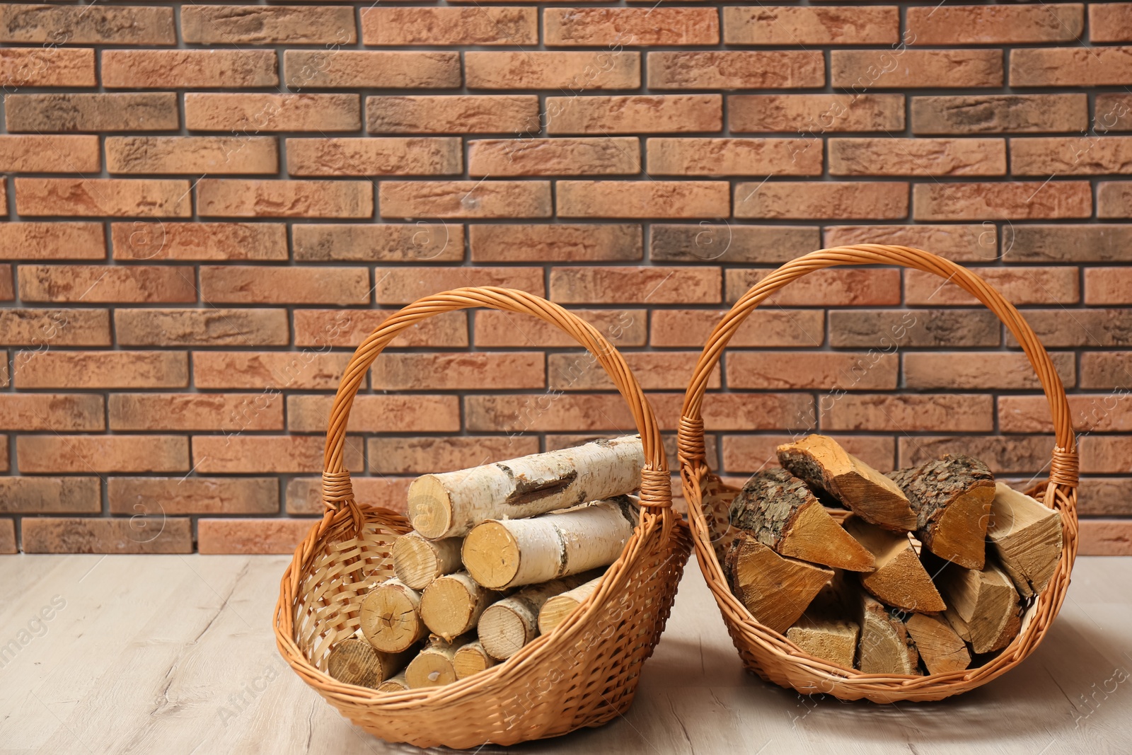 Photo of Wicker baskets with firewood near brick wall indoors