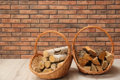 Wicker baskets with firewood near brick wall indoors