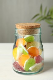 Photo of Delicious fruity gummy candies in glass jar on white wooden table