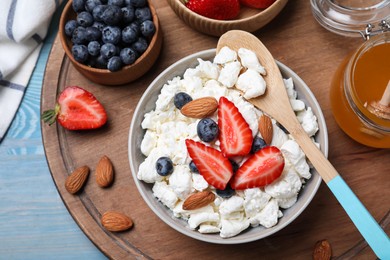 Bowl of fresh cottage cheese, berries with almond and ingredients on wooden board, flat lay