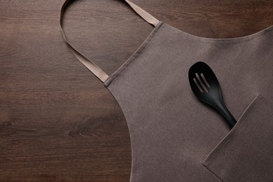 Photo of Stylish brown apron and slotted spoon on wooden table, top view. Space for text