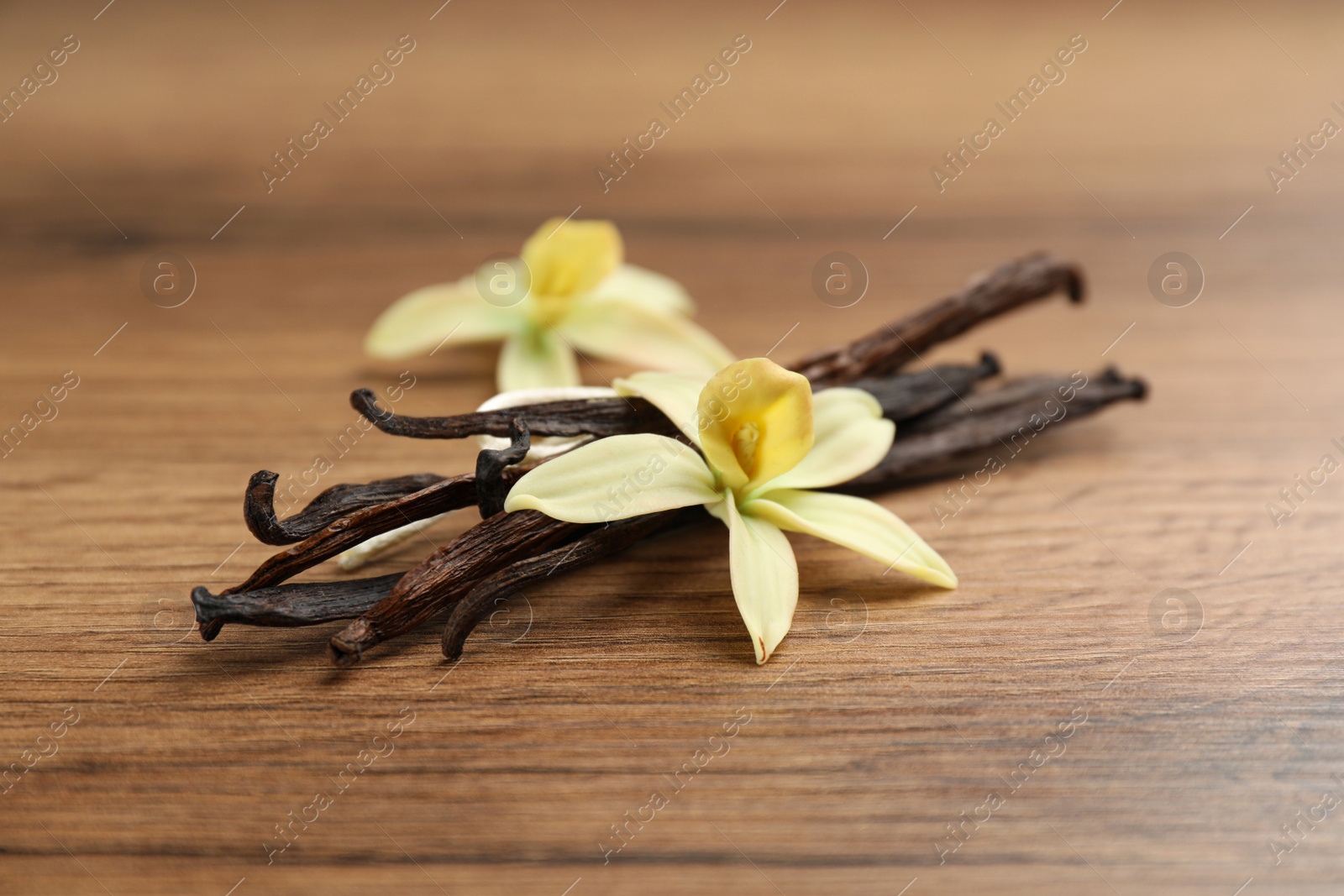 Photo of Aromatic vanilla sticks and flowers on wooden table, closeup