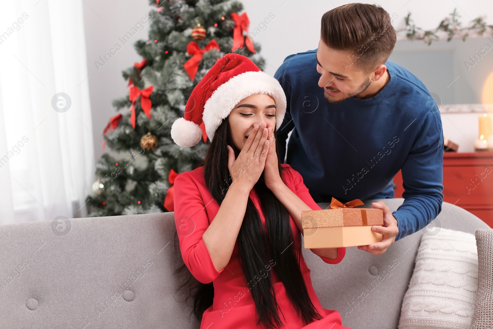 Photo of Young man giving gift box to girlfriend at home. Happy couple celebrating Christmas