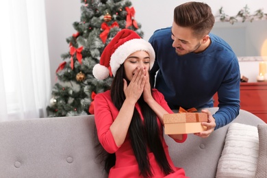 Photo of Young man giving gift box to girlfriend at home. Happy couple celebrating Christmas