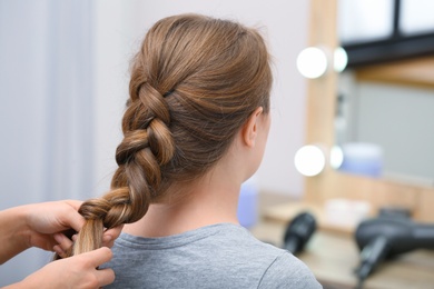 Photo of Professional coiffeuse braiding client's hair in salon