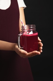 Photo of Woman with mason jar of beet smoothie on black background, closeup