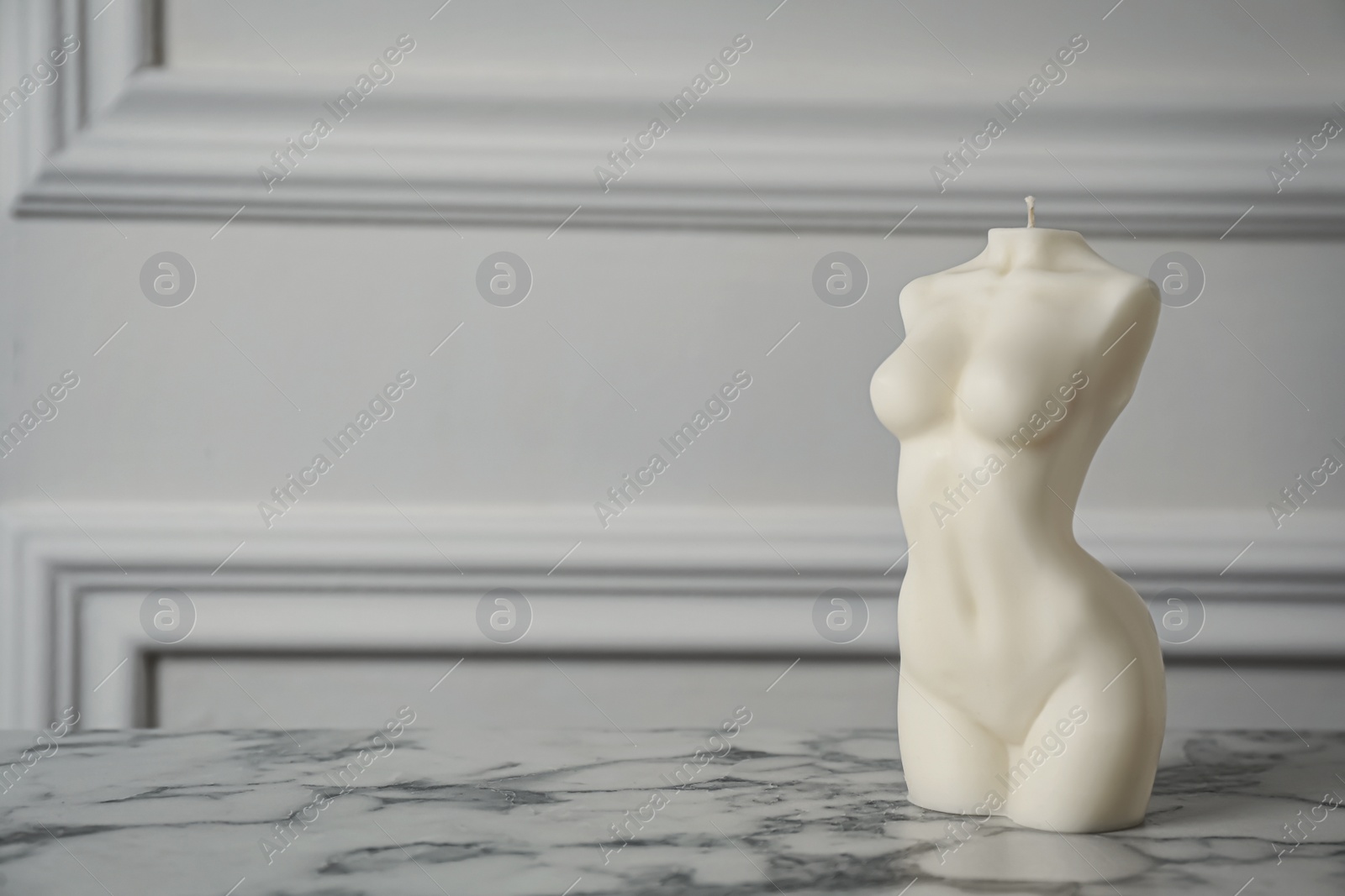 Photo of Stylish female body shaped candle on white marble table. Space for text