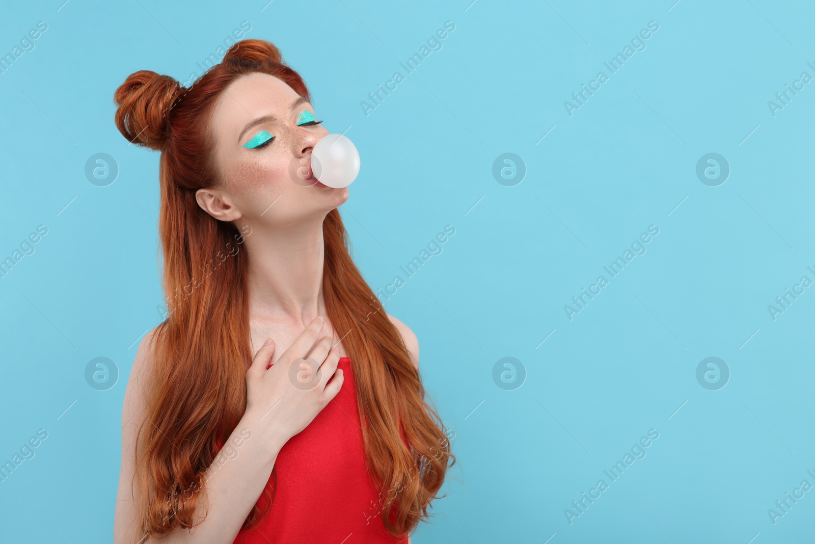 Photo of Beautiful woman with bright makeup and closed eyes blowing bubble gum on light blue background. Space for text