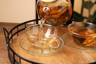 Photo of Pouring tasty tea into glass cup at wooden table, closeup