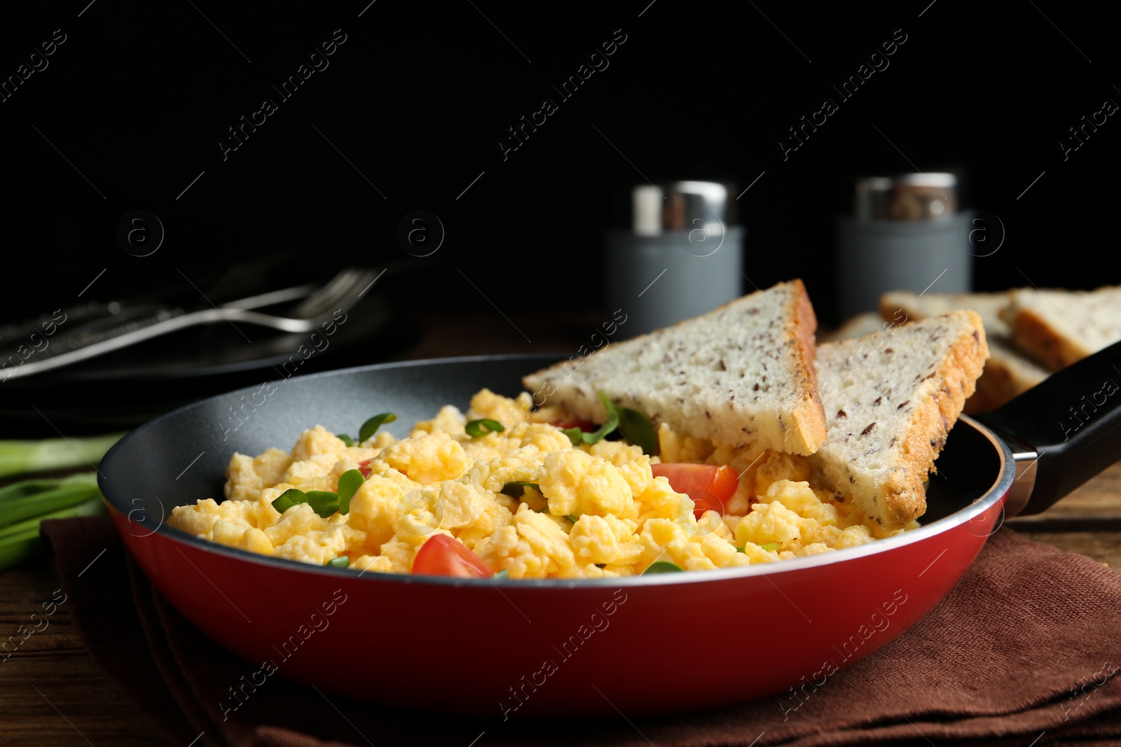 Photo of Tasty scrambled eggs with sprouts, cherry tomato and bread in frying pan on table