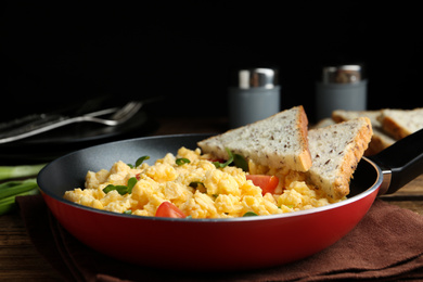 Photo of Tasty scrambled eggs with sprouts, cherry tomato and bread in frying pan on table