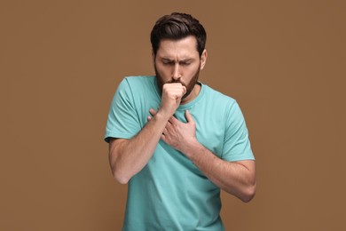 Photo of Sick man coughing on brown background. Cold symptoms