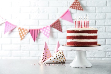 Delicious homemade red velvet cake with candles on table against brick wall. Space for text