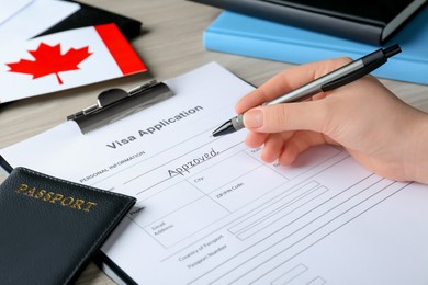 Photo of Woman filling visa application form for immigration to Canada at table, closeup