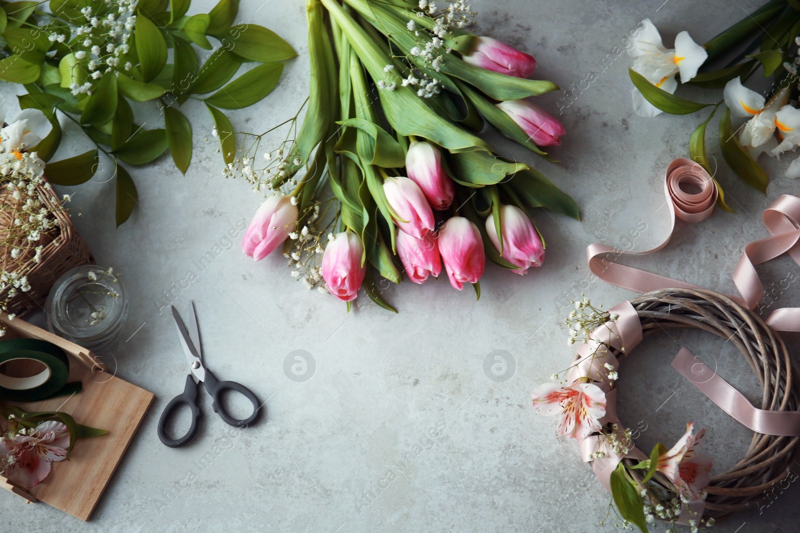 Photo of Decorator's workplace with unfinished wreath and beautiful flowers, top view