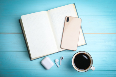 Book, coffee, earphones and mobile phone on light blue wooden table, flat lay