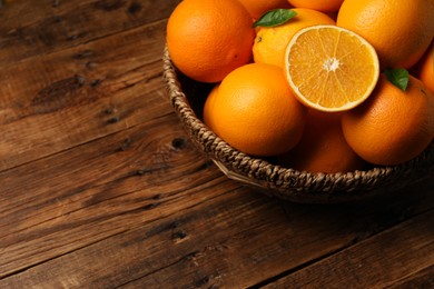 Photo of Many ripe oranges and green leaves on wooden table. Space for text