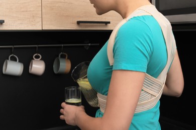 Woman with orthopedic corset pouring lemonade into glass in kitchen, closeup