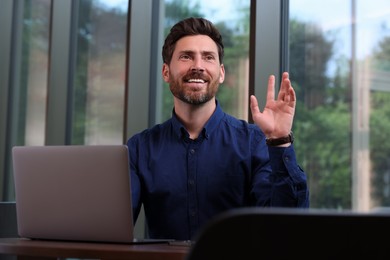 Photo of Man with laptop greeting someone at table in cafe