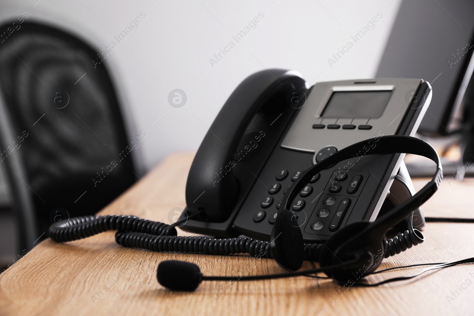 Photo of Stationary phone and headset on wooden desk in office. Hotline service