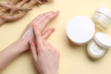 Woman applying hand cream on beige background, top view