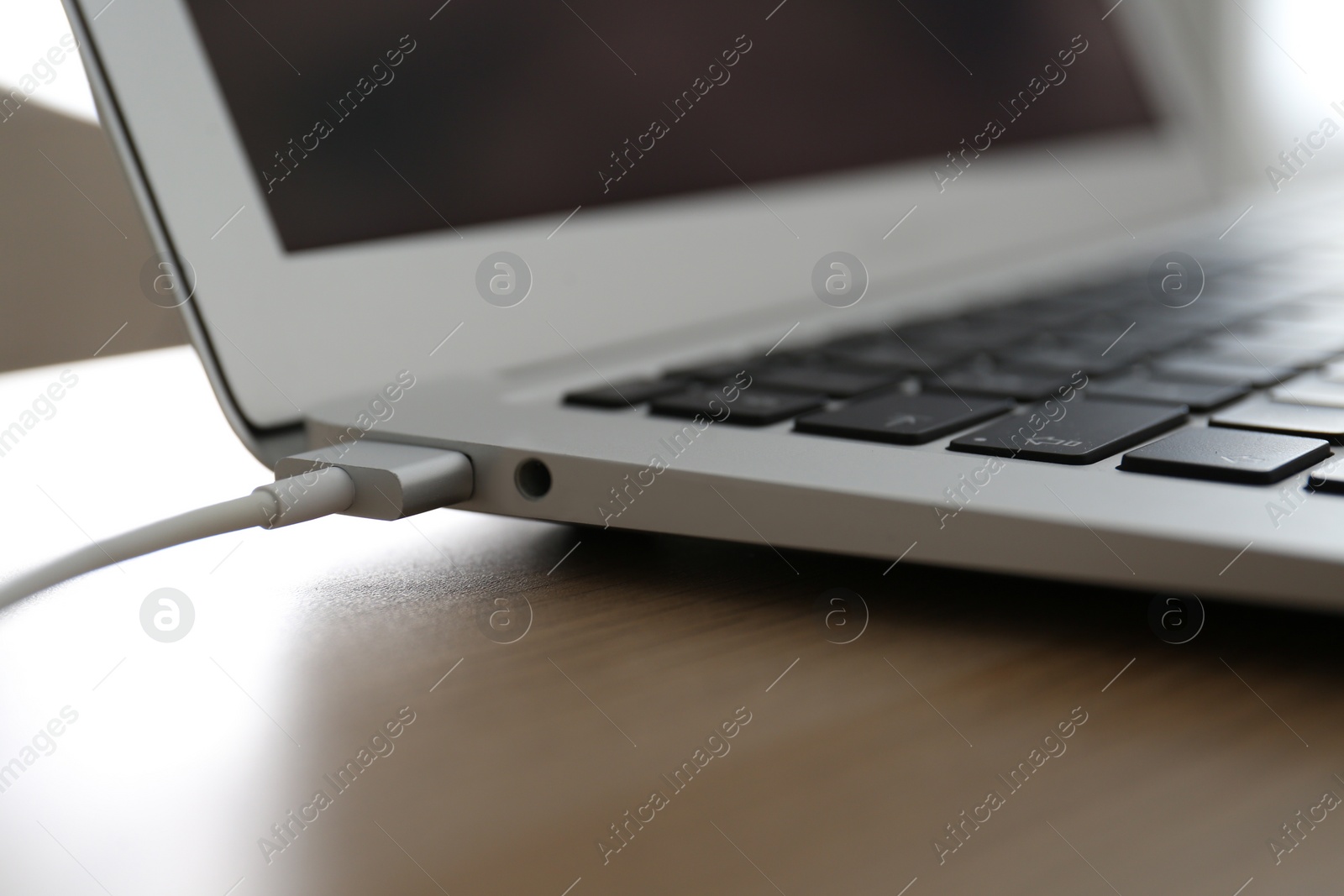 Photo of Modern laptop charging on wooden table, closeup