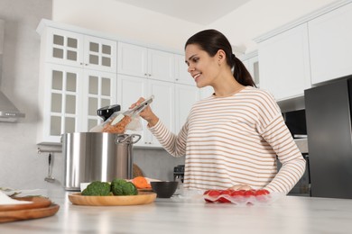 Photo of Woman putting vacuum packed meat into pot with sous vide cooker in kitchen. Thermal immersion circulator