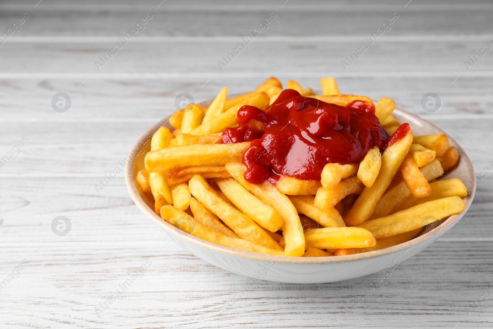 Photo of Bowl of tasty french fries on white wooden table