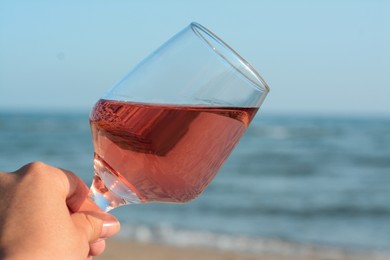 Photo of Woman holding glasstasty rose wine near sea, closeup