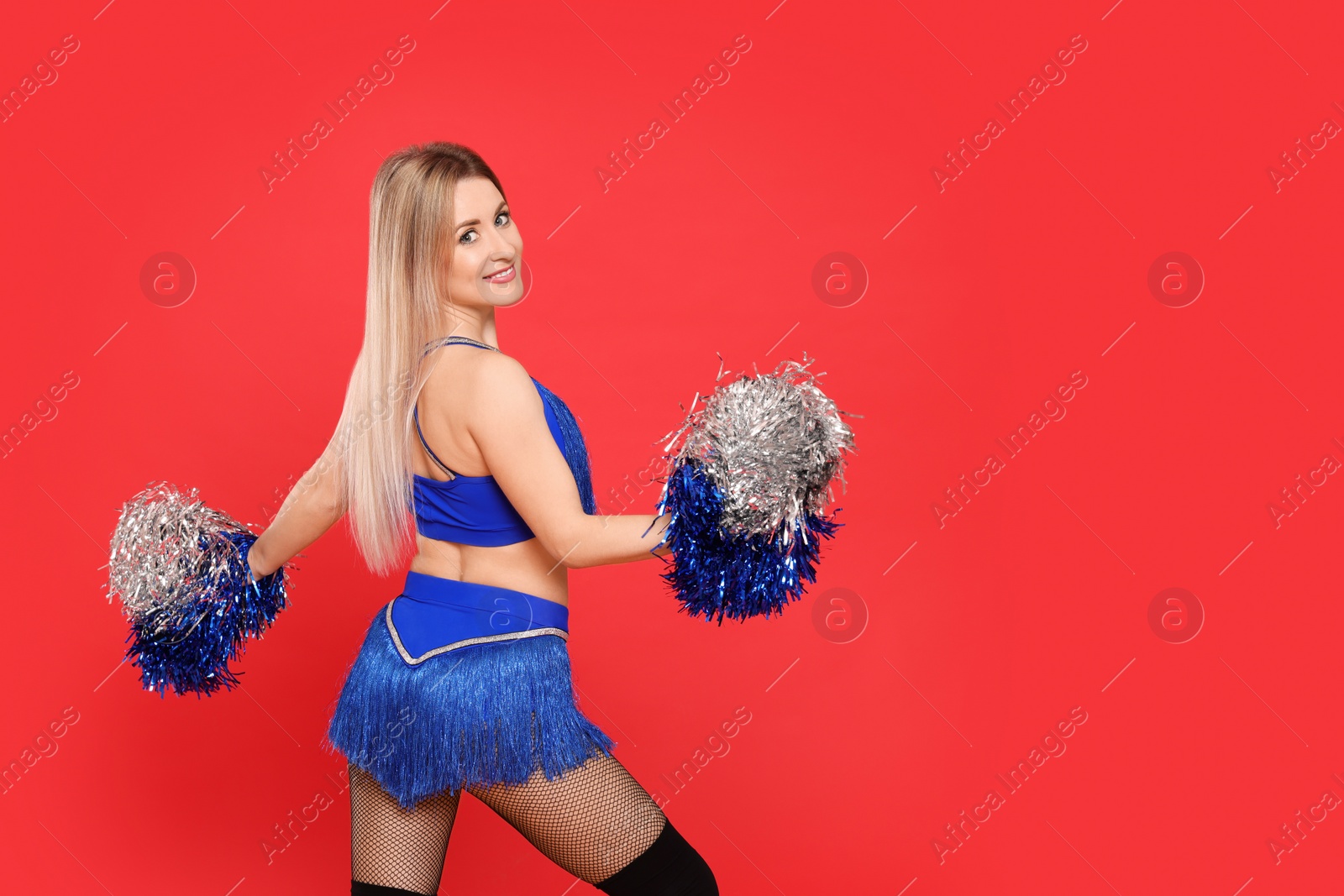 Photo of Beautiful cheerleader in costume holding pom poms on red background. Space for text