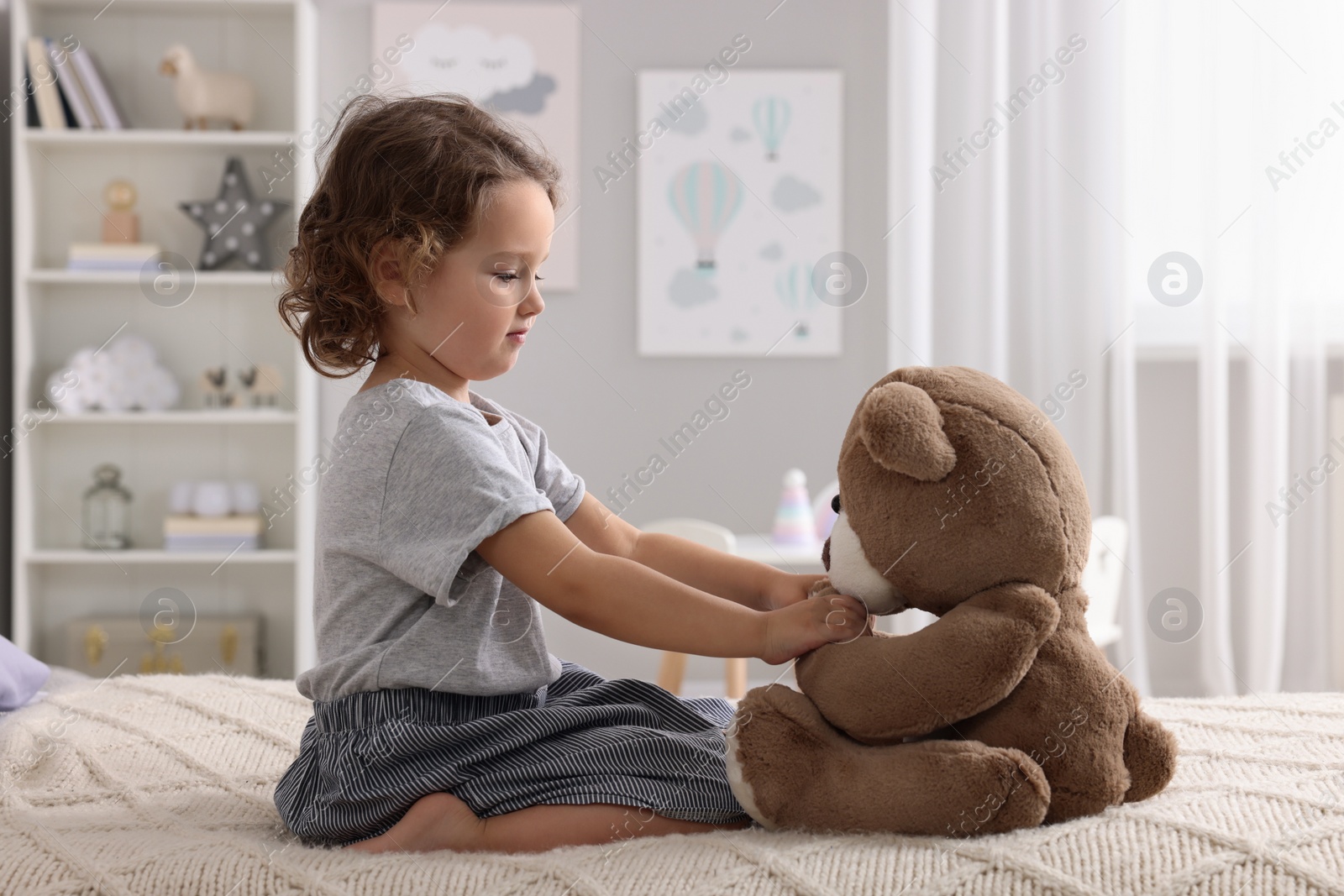 Photo of Cute little girl playing with teddy bear on bed at home