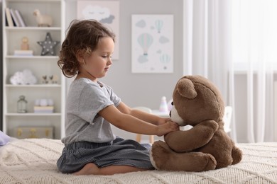Photo of Cute little girl playing with teddy bear on bed at home
